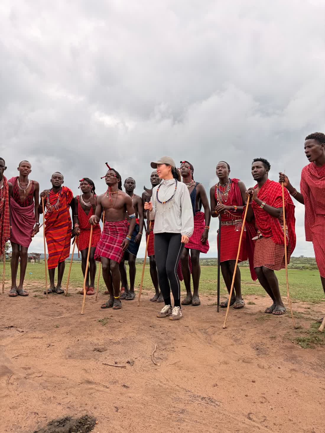 Annie Brent standing among Maasai warriors singing in red shukas