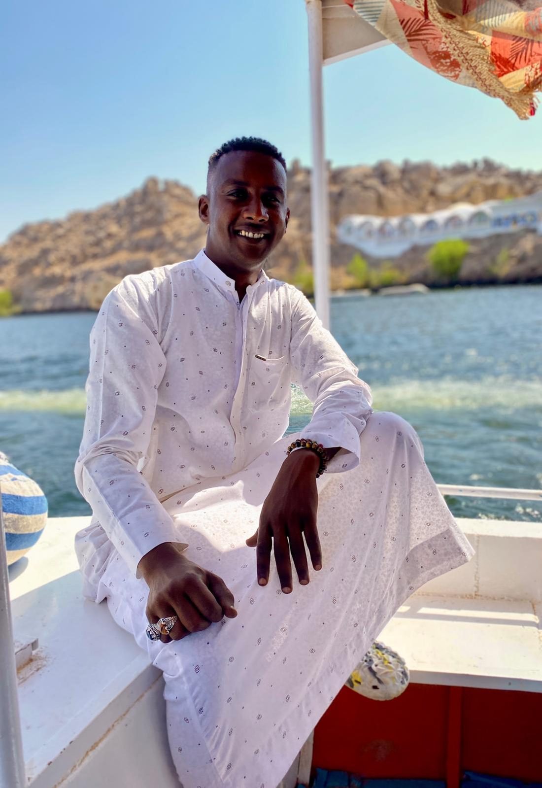 A young felucca crew member in white perched on the rail of a boat on the Nile at Aswan