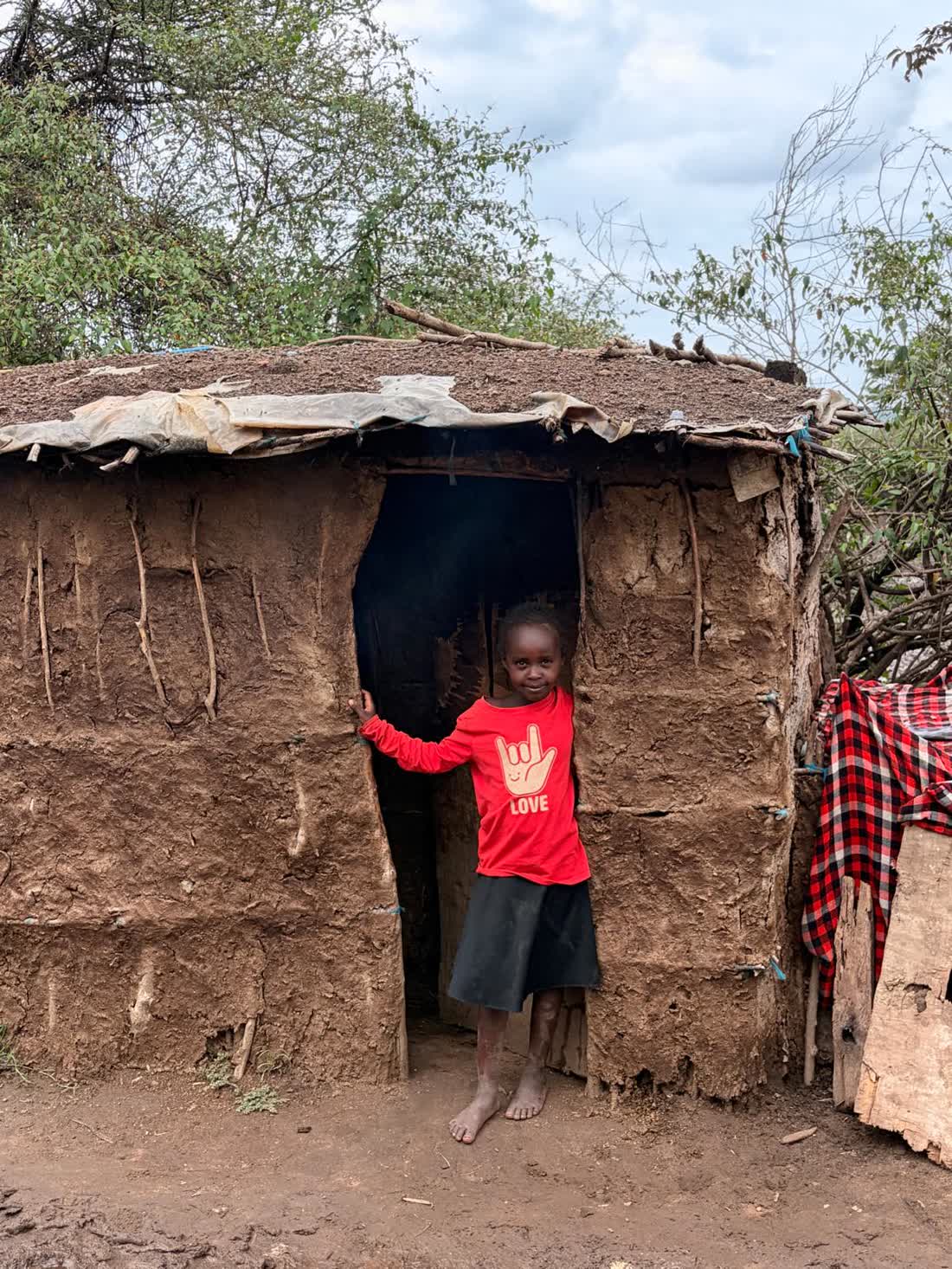 A young Maasai girl standing in the narrow doorway of a mud-walled home