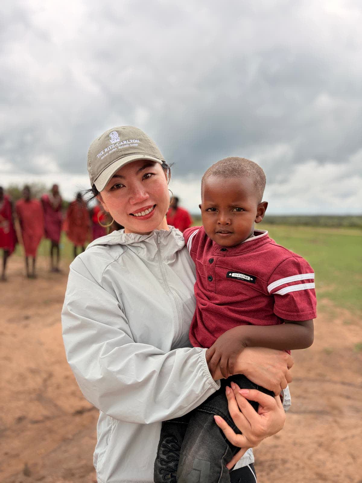 Annie Brent crouching beside a smiling Maasai child on the grass