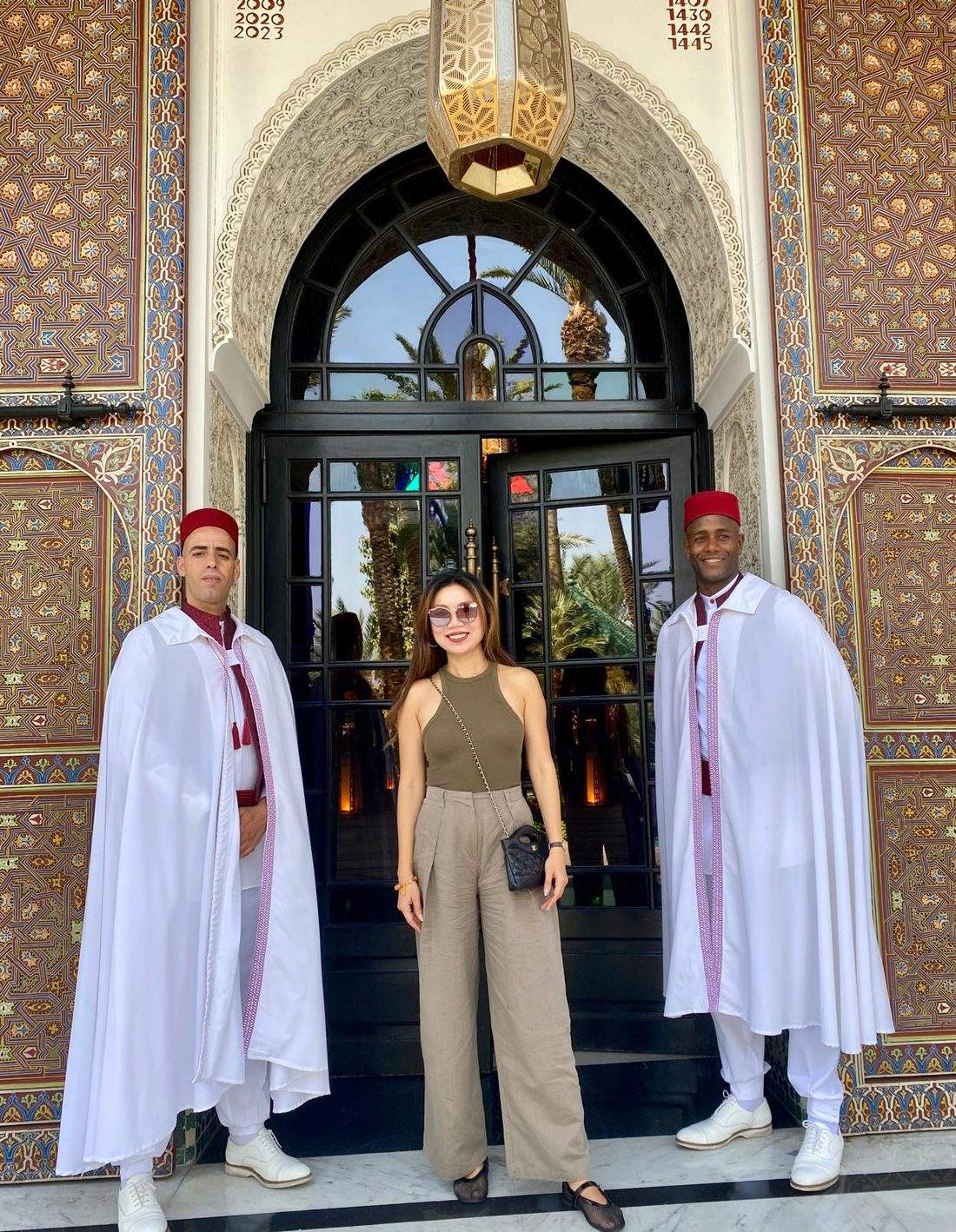Annie Brent standing between two doormen in white capes and red fezzes at an ornately tiled Marrakech entrance