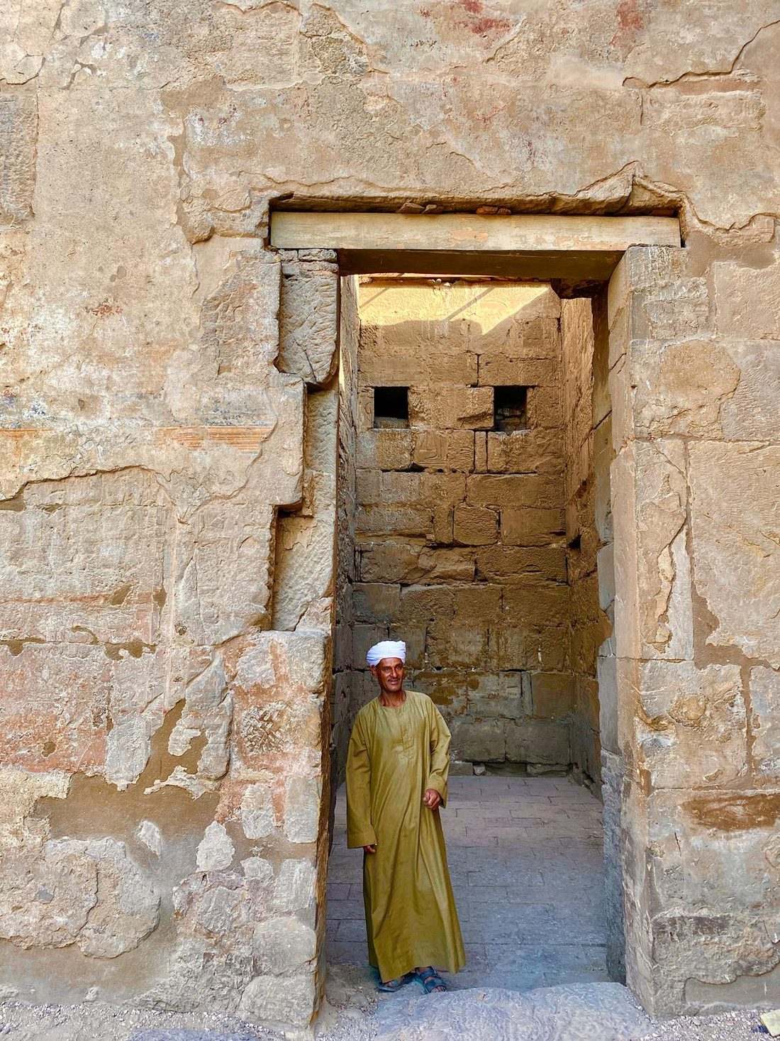 A guide in an olive galabeya standing in a weathered stone doorway at Saqqara